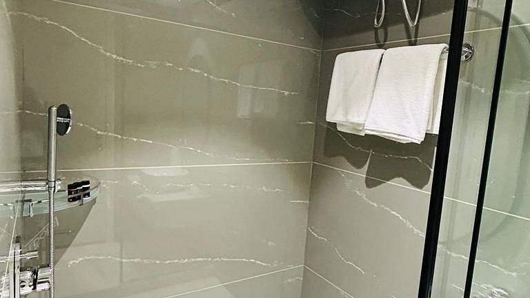 A shower enclosure with a glass door, a geyser, a towel and shower taps - Five Elements Hotels Goldleaf, Haldwani