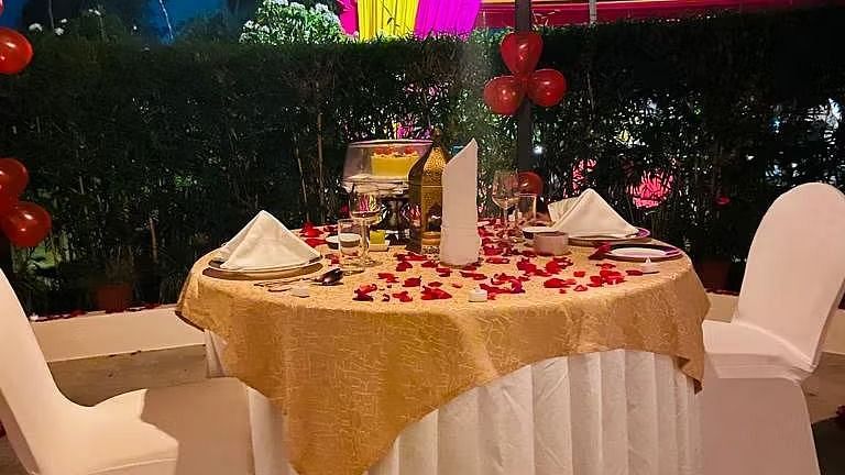 A dinner table set for two, adorned with rose petals and candles.
