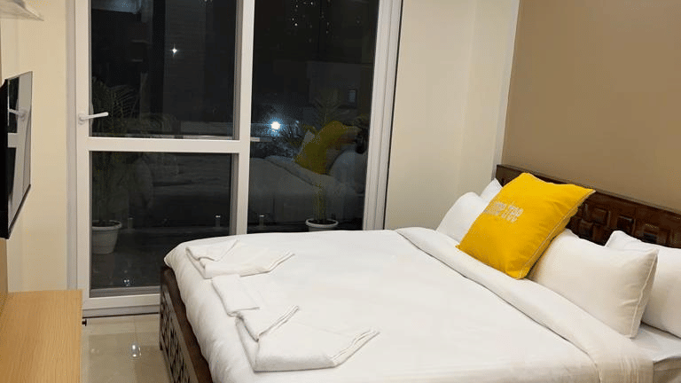 Bedroom of Lime Tree Hotels & Service Apartment Private Limited featuring yellow cushions, a curtained window, and an air conditioning unit.