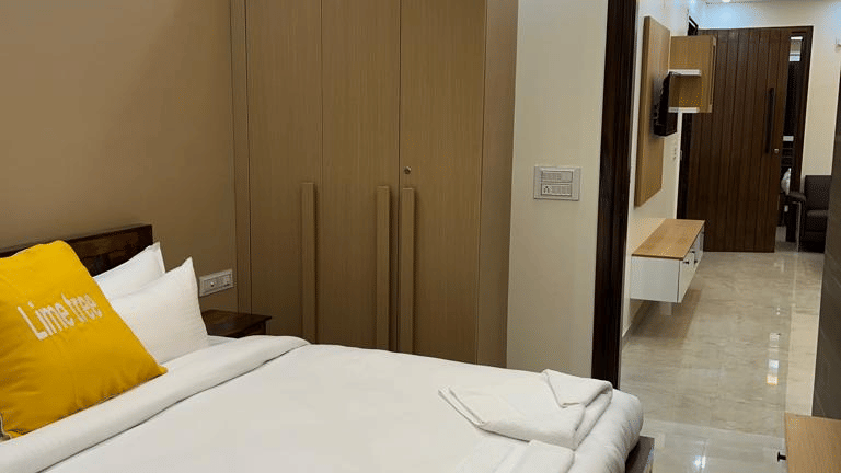 Bedroom of Lime Tree Hotels & Service Apartment Private Limited featuring yellow cushions, a wooden wardrobe, and cove lighting.