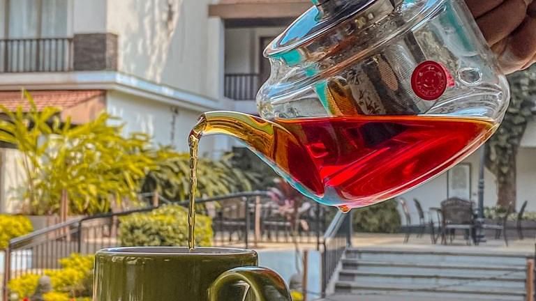Tea being poured into a green cup against the backdrop of a pool - Rhythm Lonavala