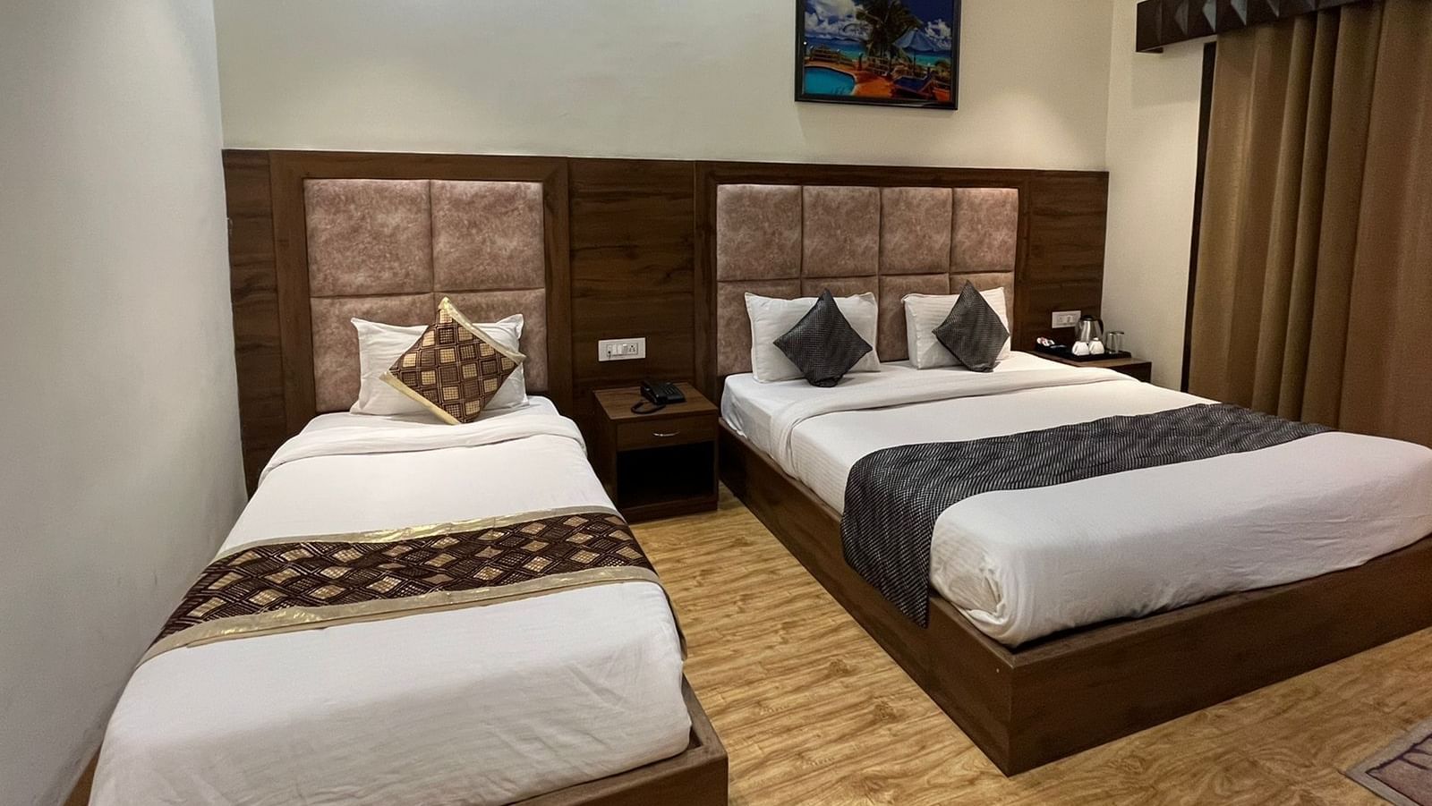 A hotel room with two beds, a queen bed and a single bed, both with matching patterned bedspreads.