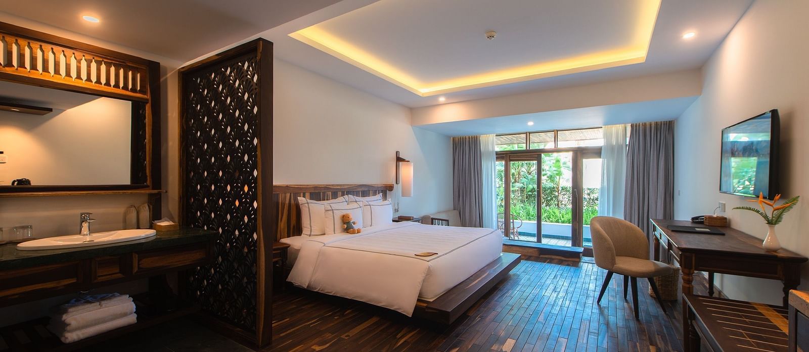 A hotel room with a king size bed, a work desk, a chair and a wall mounted television - Alibu resort Nha Trang