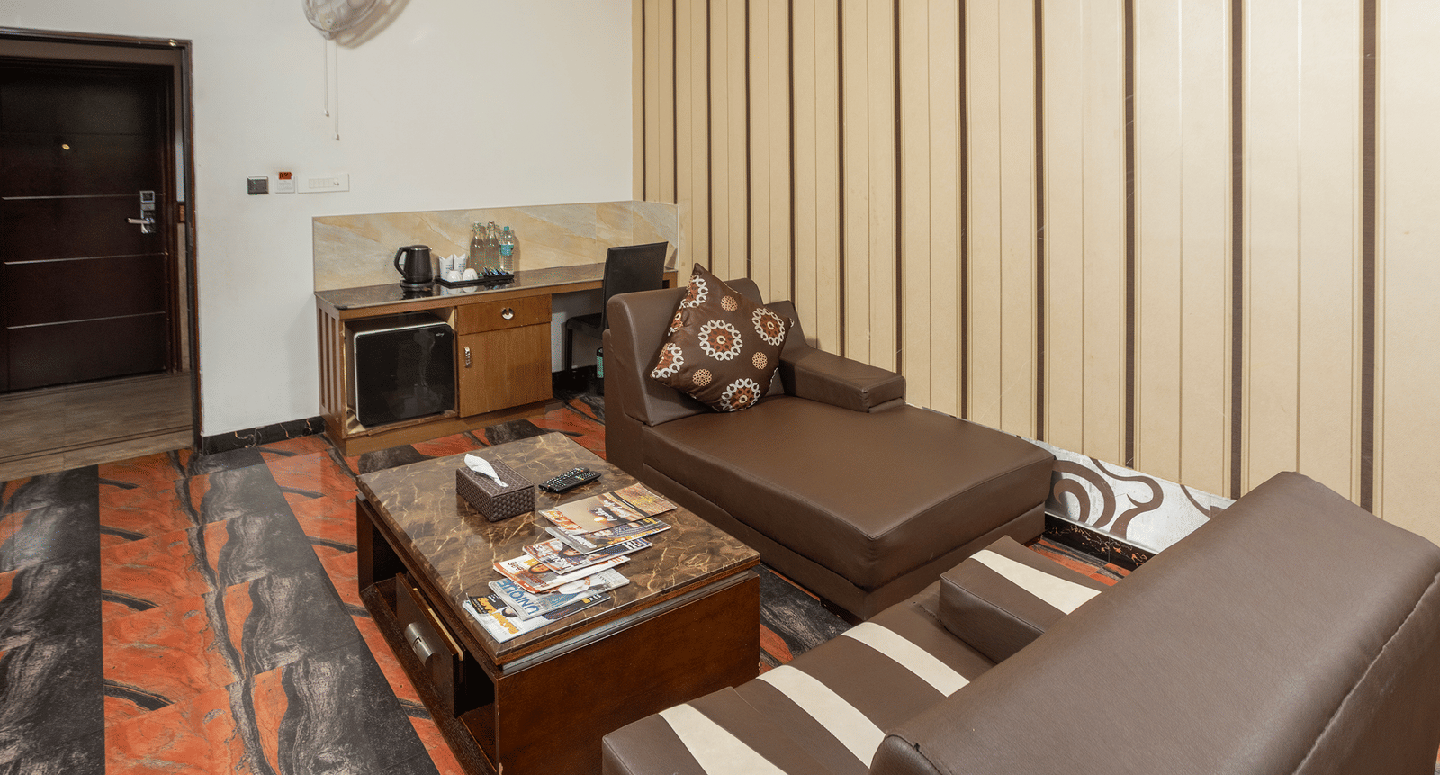 The lounge area of the Premium Room at Parakkat Nature Hotel and Resorts, Munnar featuring comfortable multi-seating sofa, a central coffee table, a small beverage counter, and a vertically-panelled accent wall.