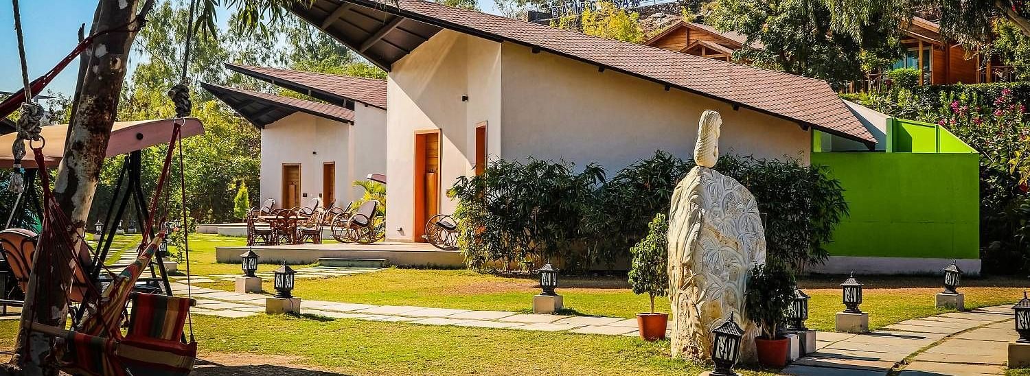 A modern building with a sloping roof sits amidst lush greenery.- Bamboo Saa Resort & Spa, Udaipur