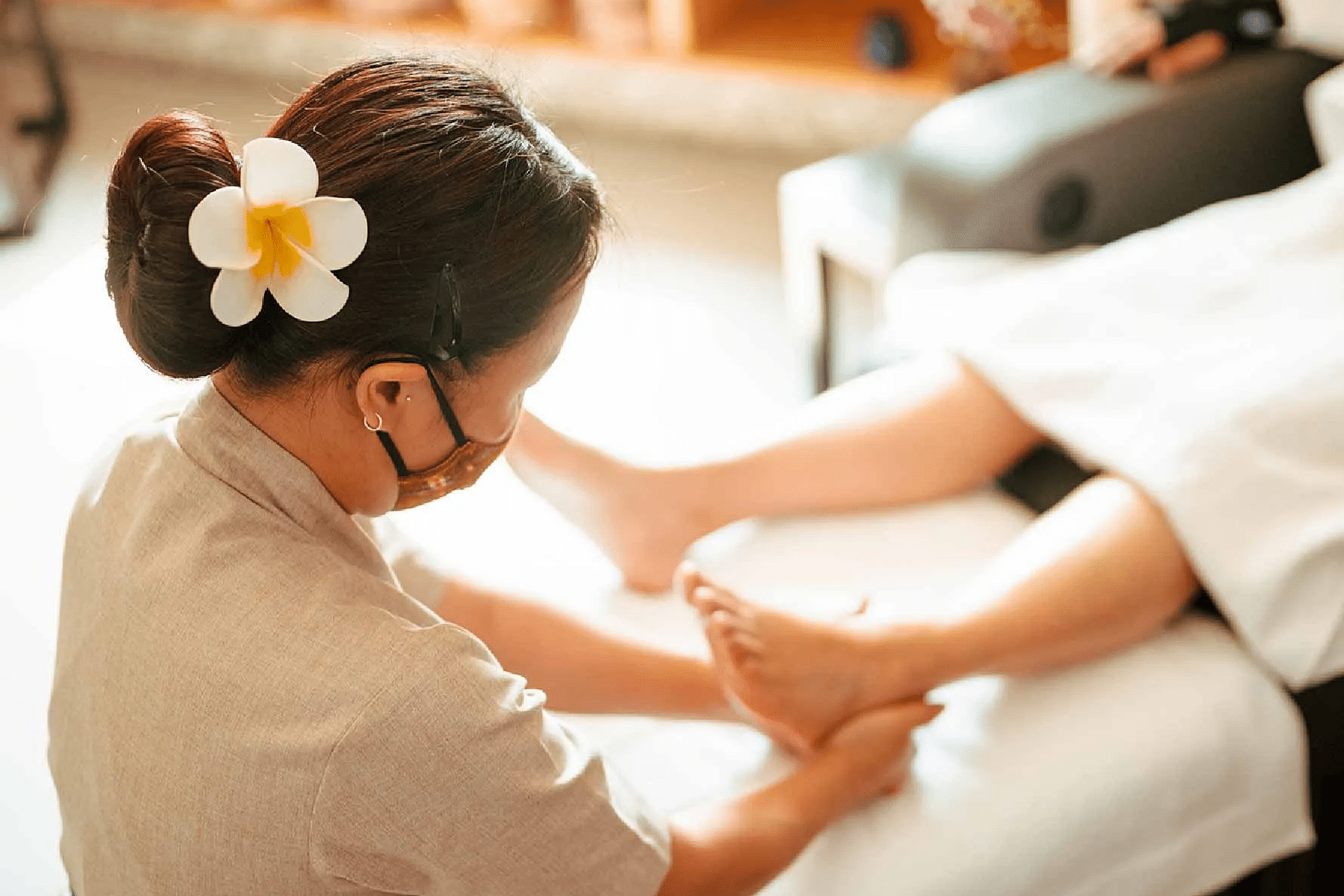 Spa therapist giving a leg massage to a client lying on a white massage bed with wooden shelves in the background at Karma Chalets.