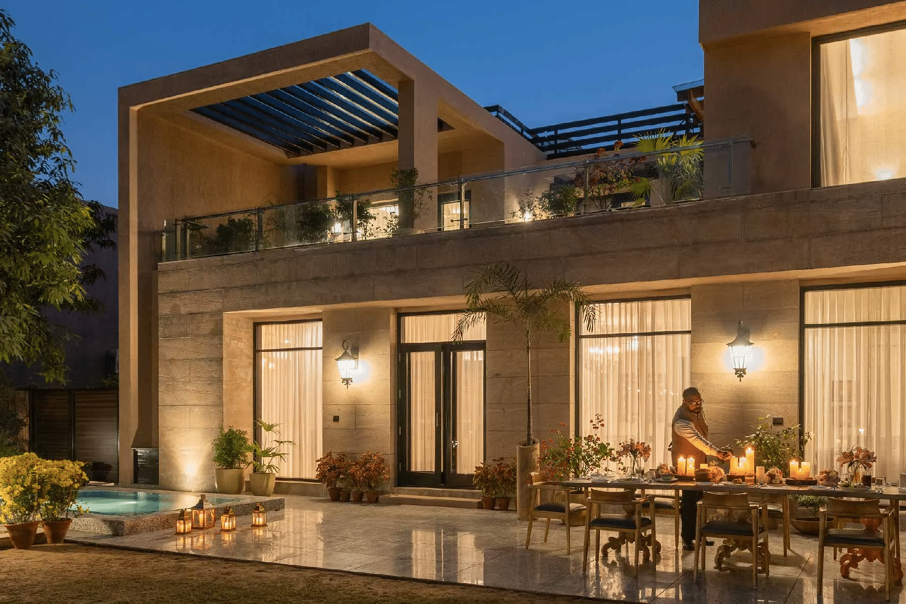 Modern two-storey house lit warmly at night, with large glass doors and an outdoor dining space at Karma Chalets.