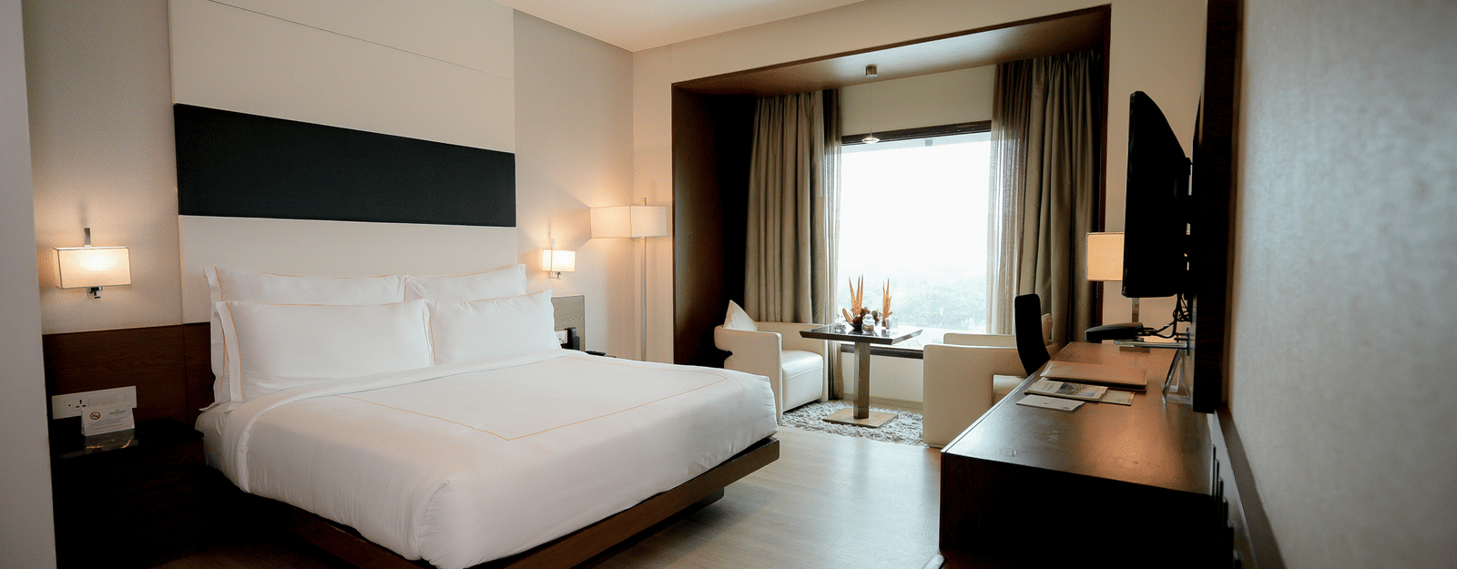 Executive suite featuring a king size bed facing tv TV on the wall next to a seating space by a large window at Narayani Heights Hotel & Resorts