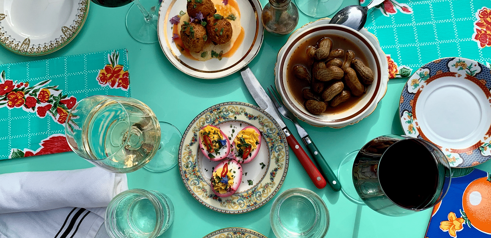 Overhead view of a table set with plates of food, glasses, utensils, and decorative fabric.