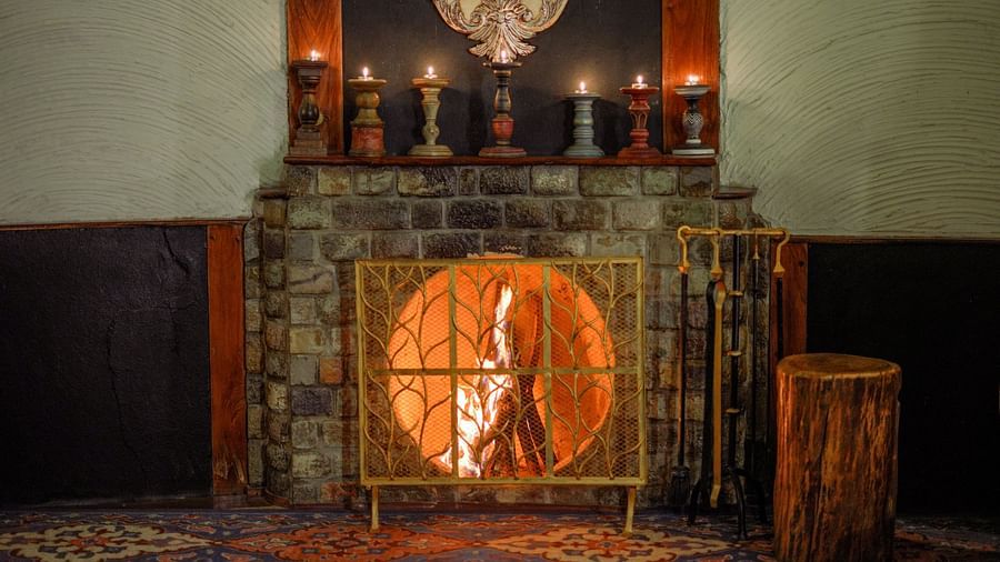 A fireplace with lit candles, a rug, and a wooden stool, warm lighting - The Den Corbett Resort & Spa, Kumeria.