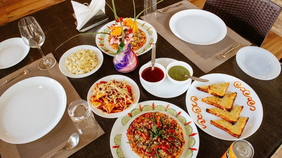 A dining table is set with 3 plates of a curry dish, toast, pasta, and sauces, at Daksh Resort & Amusement Park, Sasan Gir.