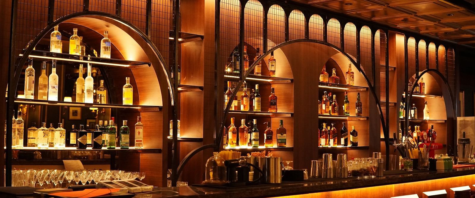 A dimly lit bar with a wooden counter, shelves filled with bottles of liquor, and warm lighting.