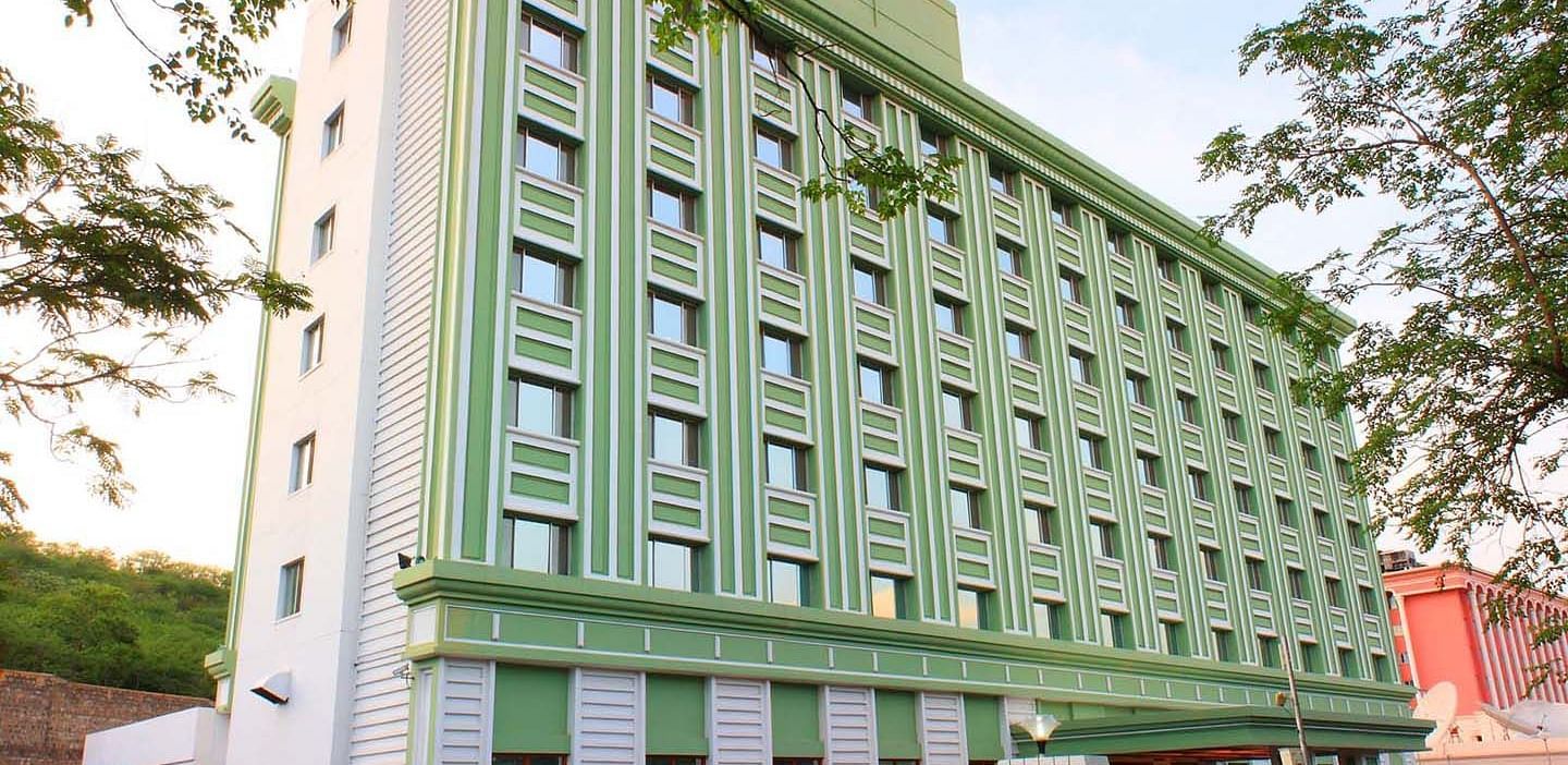 A multi-story green hotel building flanked by trees at Tara, Comfort Hotel in Hyderabad - Ramoji Film City.
