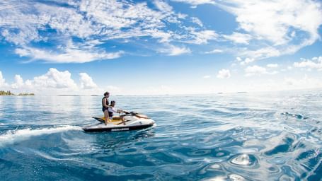 A couple in a motor boat cruising through the lake. At the horizon there are some trees and up above there is a bright sky.