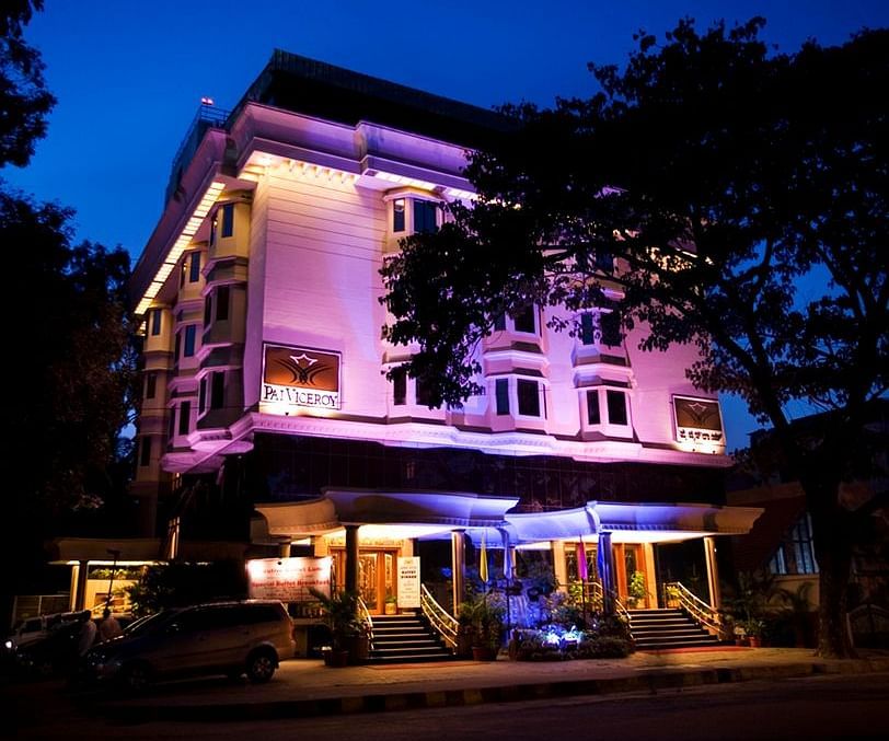 An image of a well lit facade during the night with a backdrop of trees around - Hotel Pai Viceroy Jayanagar Bangalore