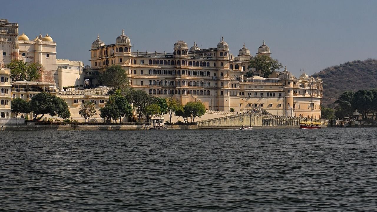 The grand City Palace complex of Udaipur, one of the most iconic places to visit in Udaipur, set against the shimmering backdrop of Lake Pichola with a partially visible hill.