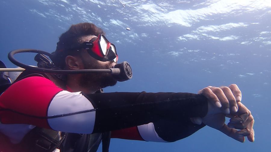 Barefoot Scuba Resort | Diver holding their wrist underwater, while surrounded by clear blue ocean water