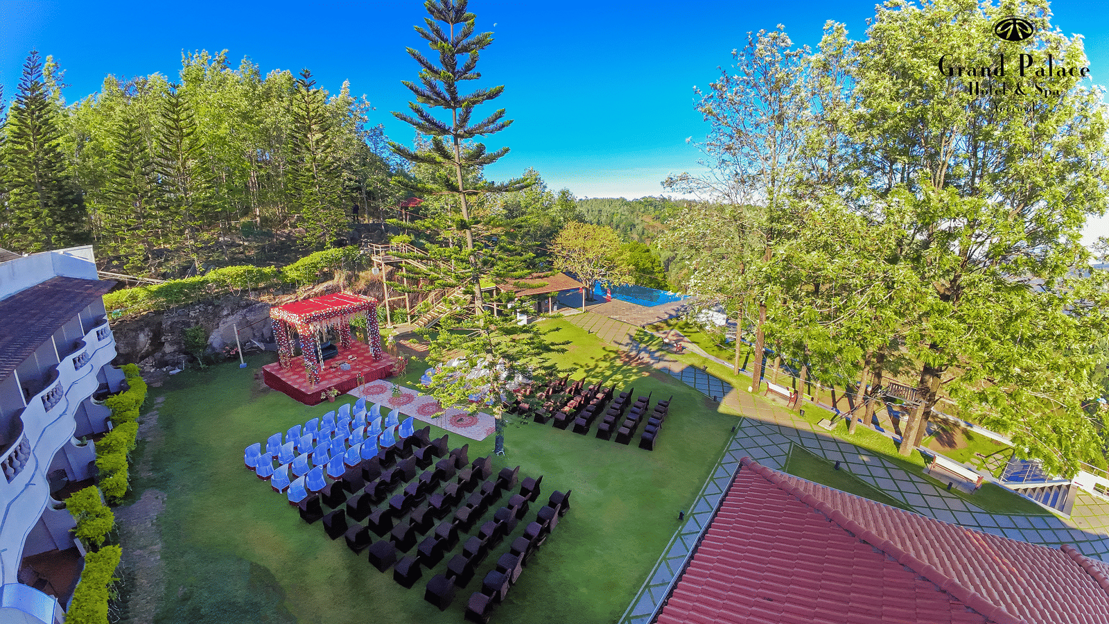 Lawn and trees with outdoor seating arrangement, flowerbeds, and children’s rides at Grand Palace, Yercaud, as seen from above.