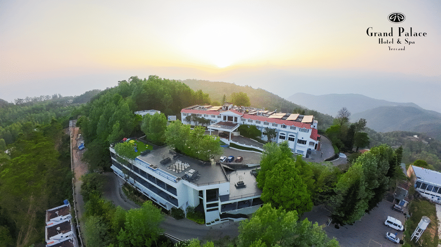 Aerial view of Grand Palace, Yercaud, showing multi-level hotel structure, driveway, parking, and tall trees.
