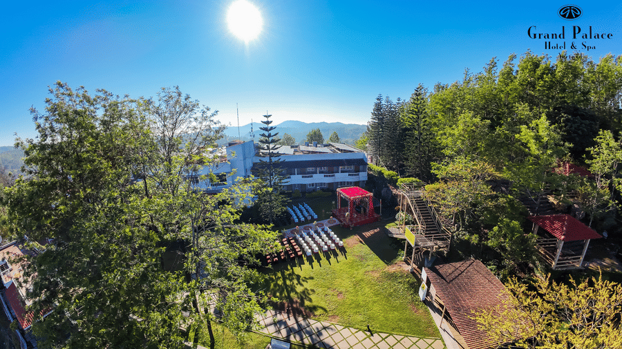 Garden view at Grand Palace, Yercaud, including seating area, grassy lawns, pathways, trees, and main building in background.