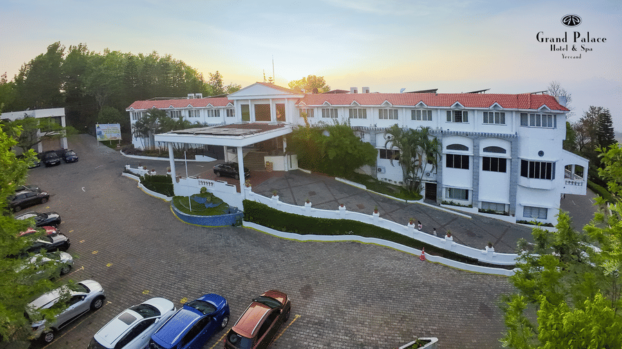 Grand Palace, Yercaud showing wide hotel facade, driveway entrance, parked vehicles, green boundary trees and exterior layout in daylight.
