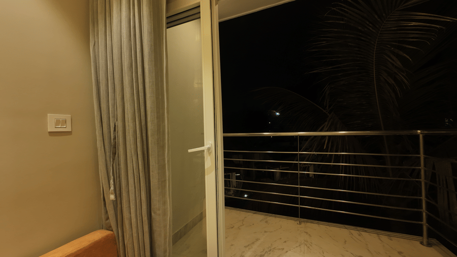  A view from Deluxe Classic Triple Bed Varanda Room  looking out through a glass door onto a dark outdoor balcony with a metal railing in night at Hotel Seagull Digha