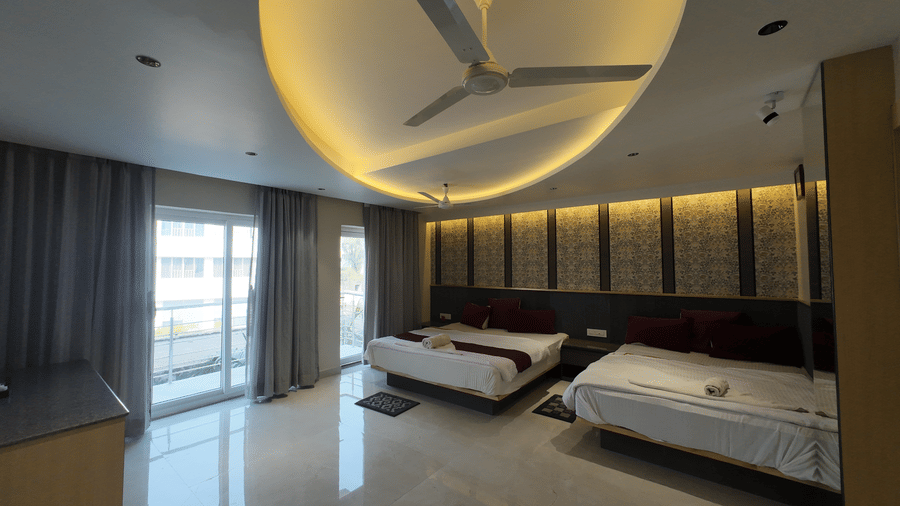 Deluxe Classic 4 Bedded Varanda Room featuring two beds, a curved false ceiling with warm yellow cove lighting, and a large window with curtains at Hotel Seagull Digha