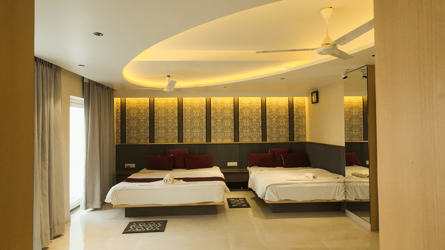 Deluxe Classic 4 Bedded Varanda Room featuring two beds, a curved false ceiling with warm yellow cove lighting, and a large window with curtains at Hotel Seagull Digha