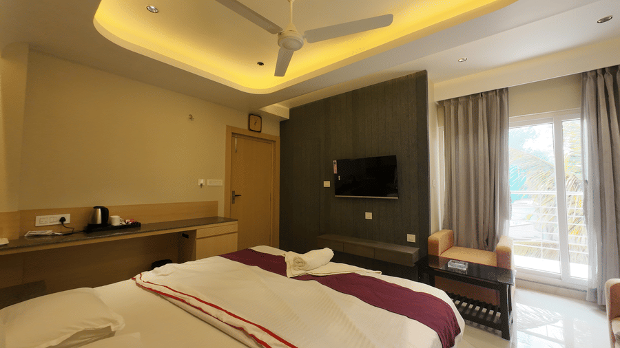 Deluxe Classic Triple Bed Varanda with a large bed, a wooden desk, a wall-mounted television, and warm cove lighting at Hotel Seagull Digha