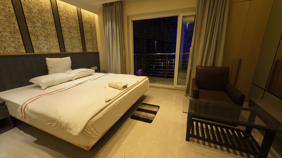 Deluxe Classic Varanda Room at night with a large bed, armchair, and a view of the outside through a sliding glass door at Hotel Seagull Digha