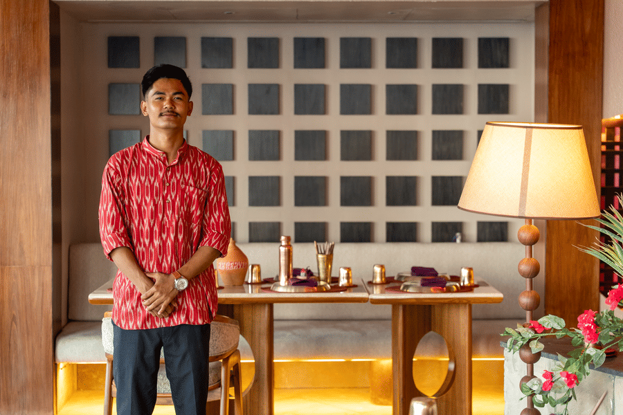 Staff member standing inside Jamun restaurant beside a table setup and decorative lighting - Symphony Resorts