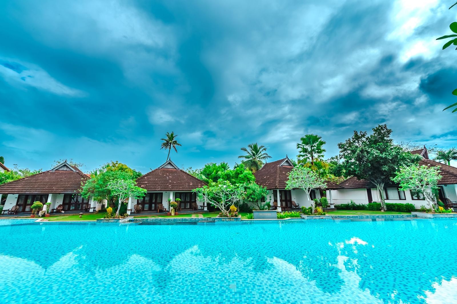 an image of cluster of cottages surrounded by a big swimming pool - Rhythm Kumarakom