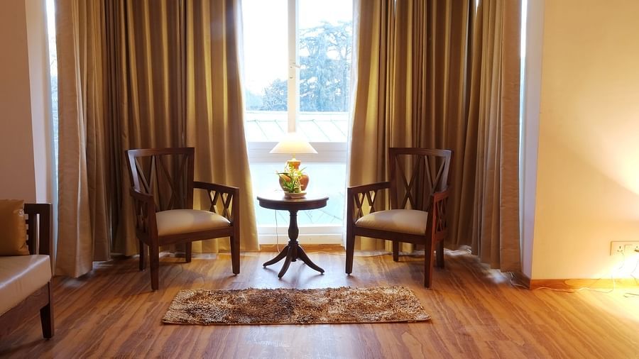 A cozy hotel room with warm lighting, featuring comfortable seating and a view through large windows.