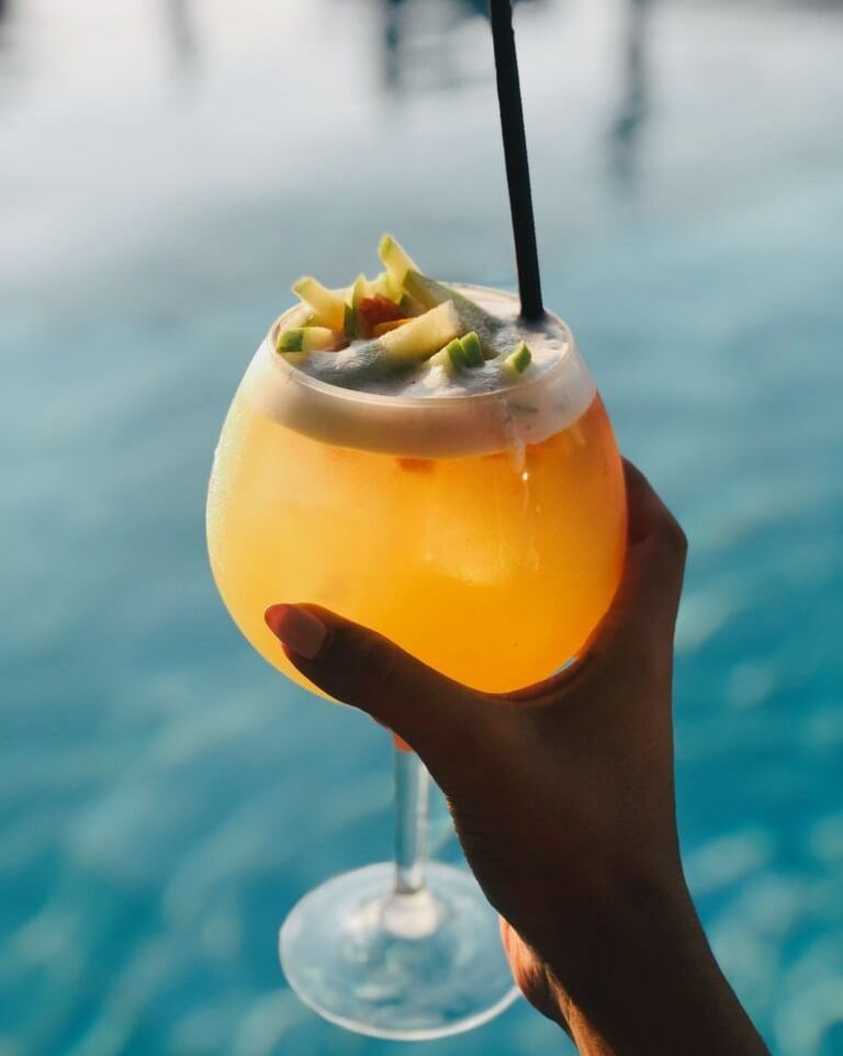 A person holding a vibrant looking beverage over a swimming pool at Tamarind Hills Resorts and Villas, Antingua.