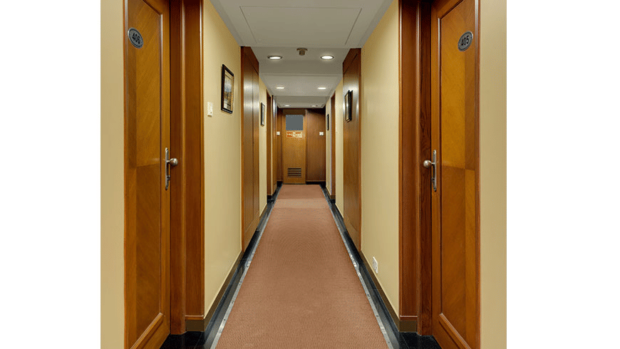 A carpeted hotel corridor lined with wooden doors on both sides | Trance Oakwood Hotel, Pune