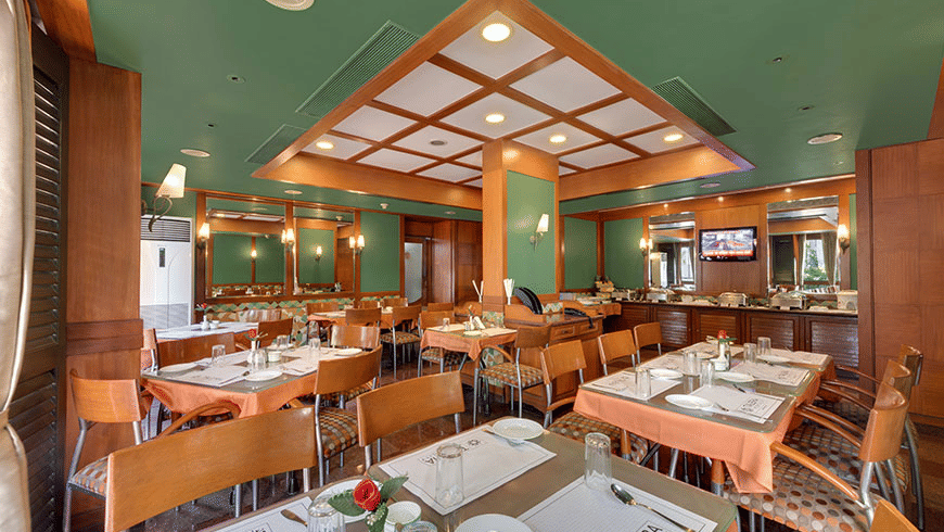 A restaurant dining room with wooden furniture and set tables under a recessed ceiling | Trance Oakwood Hotel, Pune