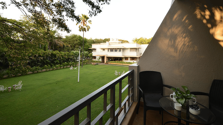 View from a balcony at Trance Sunderban Resort showing black chairs, a small table, and a railing overlooking a large, manicured green lawn.