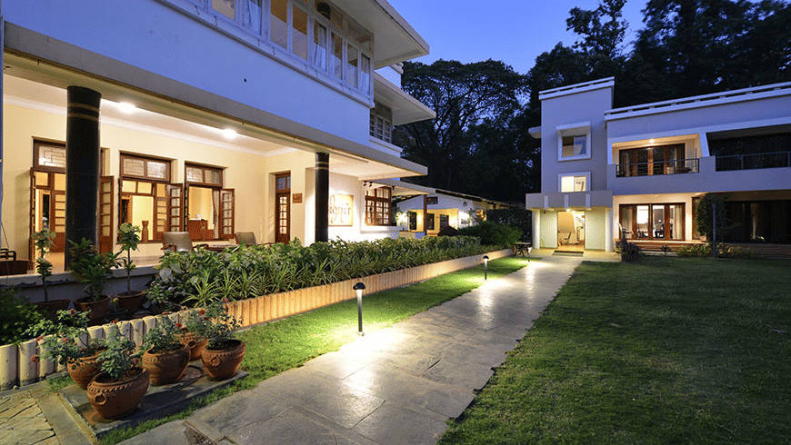 The exterior of Trance Sunderban Resort at night, showing lit doorways and windows overlooking a dark green lawn.