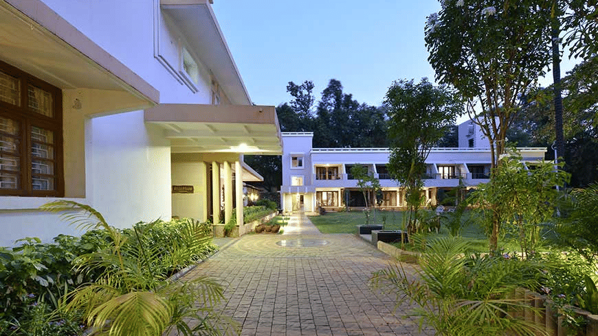 Exterior of Trance Sunderban Resort at dusk featuring 2 buildings, manicured garden beds, and a stone-paved pathway.