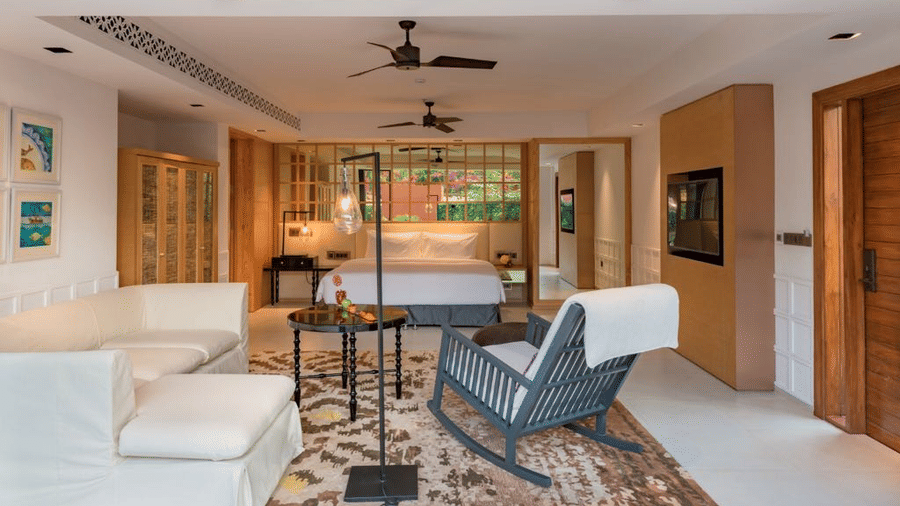 Room with a blue rocking chair and couches in front of a plush bed under warm lighting at Azaya Beach Resort Goa
