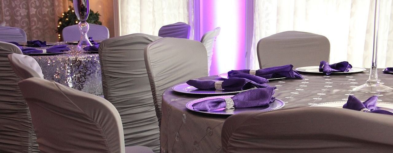 An image of a banquet hall showcasing elegantly arranged round tables with beautifully decorated chairs.