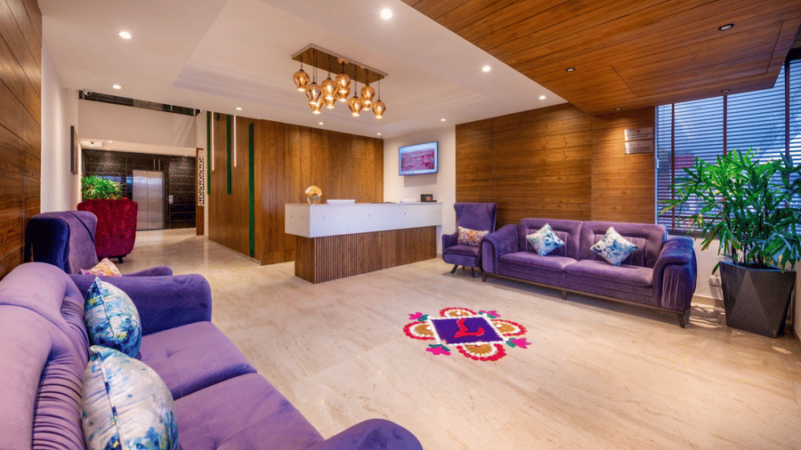 Spacious hotel reception with colourful cushioned sofas, wooden accents, chandeliers, and large windows.