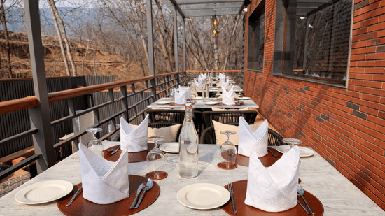 Outdoor seating area at Noor All-day Dining in Mountnoor Sarovar Premiere, Pahalgam, featuring set tables neatly arranged along safety railings offering views of the hills and the surroundings.