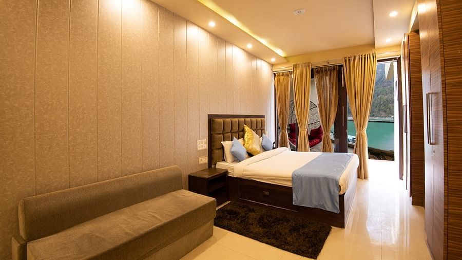 Spacious room featuring a bed, wall-mounted TV, sofa, and balcony view through glass doors.