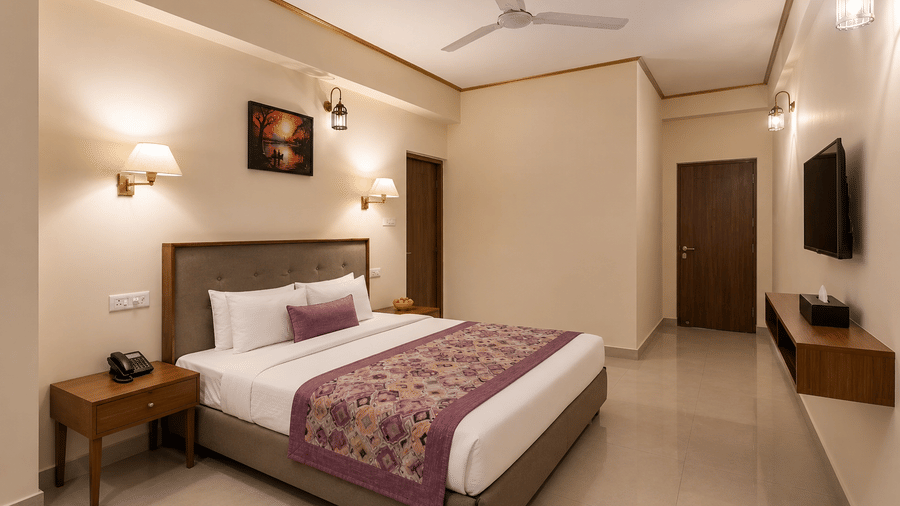 Family Room at Valmere Himalayan Hotel & Spa, Gangtok with a king-size bed, framed artwork above the headboard, and a hallway leading to a wall-mounted TV.