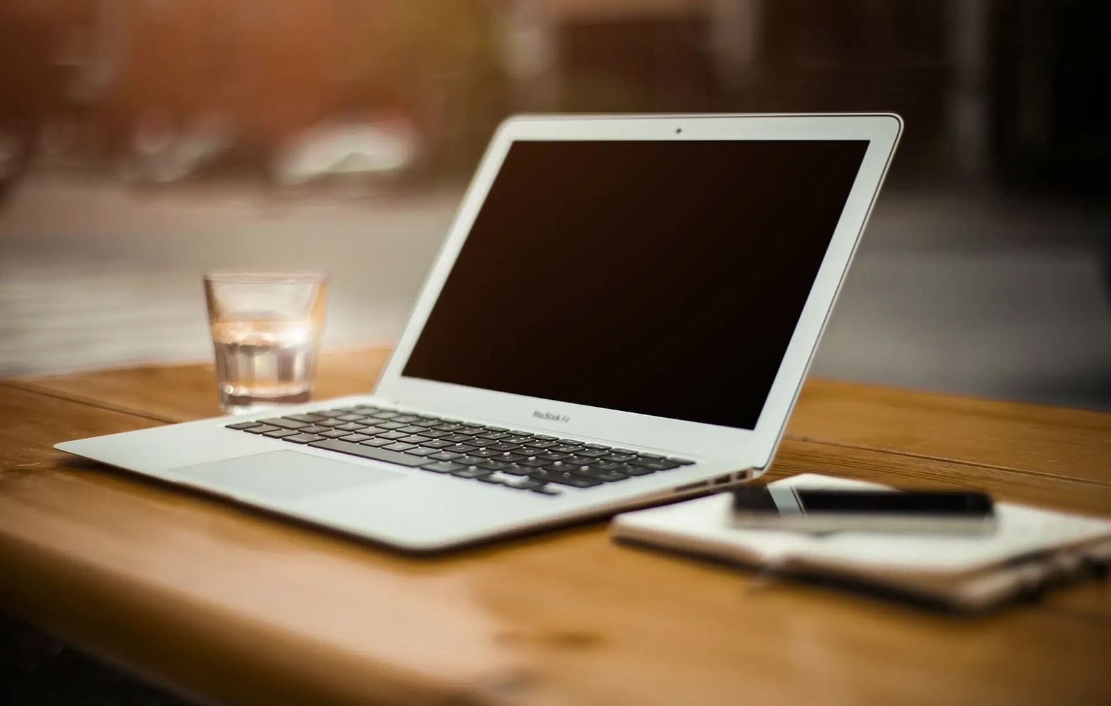 A laptop and a notebook with a pen are placed on a wooden desk.