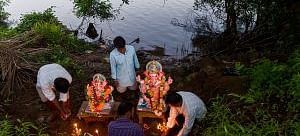 Several people are gathered near a body of water, preparing to immerse idols.