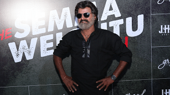 Celebrity posing at an event with a backdrop featuring branding and text.
