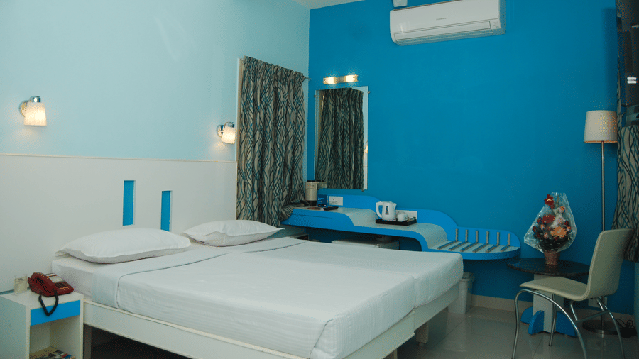 A bright hotel room with twin beds pushed together against a striking blue accent wall next to a dressing mirror setup - Hotel Pandian