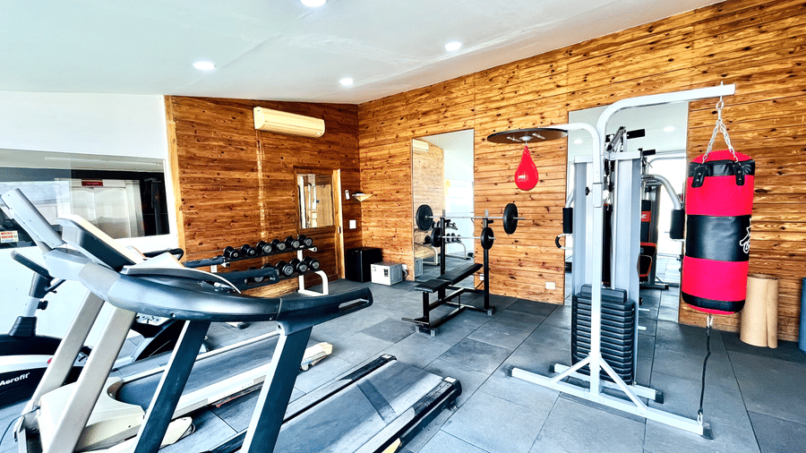 Inside a modern gym with wood paneling, featuring treadmills, a multi-gym weight machine, and a red punching bag.